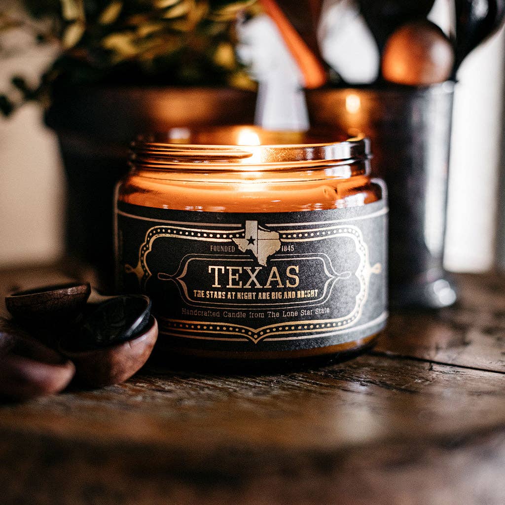 Jackson Vaughn Texas Candle – lit amber candle jar on a wooden table