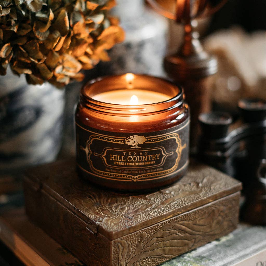 Jackson Vaughn Texas Hill Country Candle – lit wide amber candle jar on a wooden box