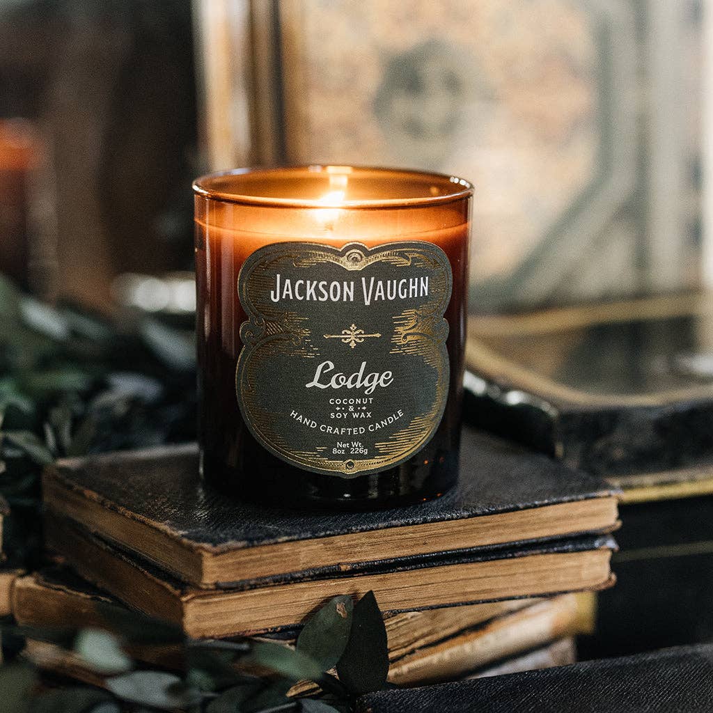 Jackson Vaughn Lodge Candle – lit amber candle jar on stacked books