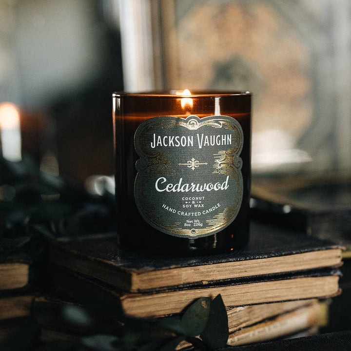 Jackson Vaughn Cedarwood Candle – lit amber candle jar on stacked books